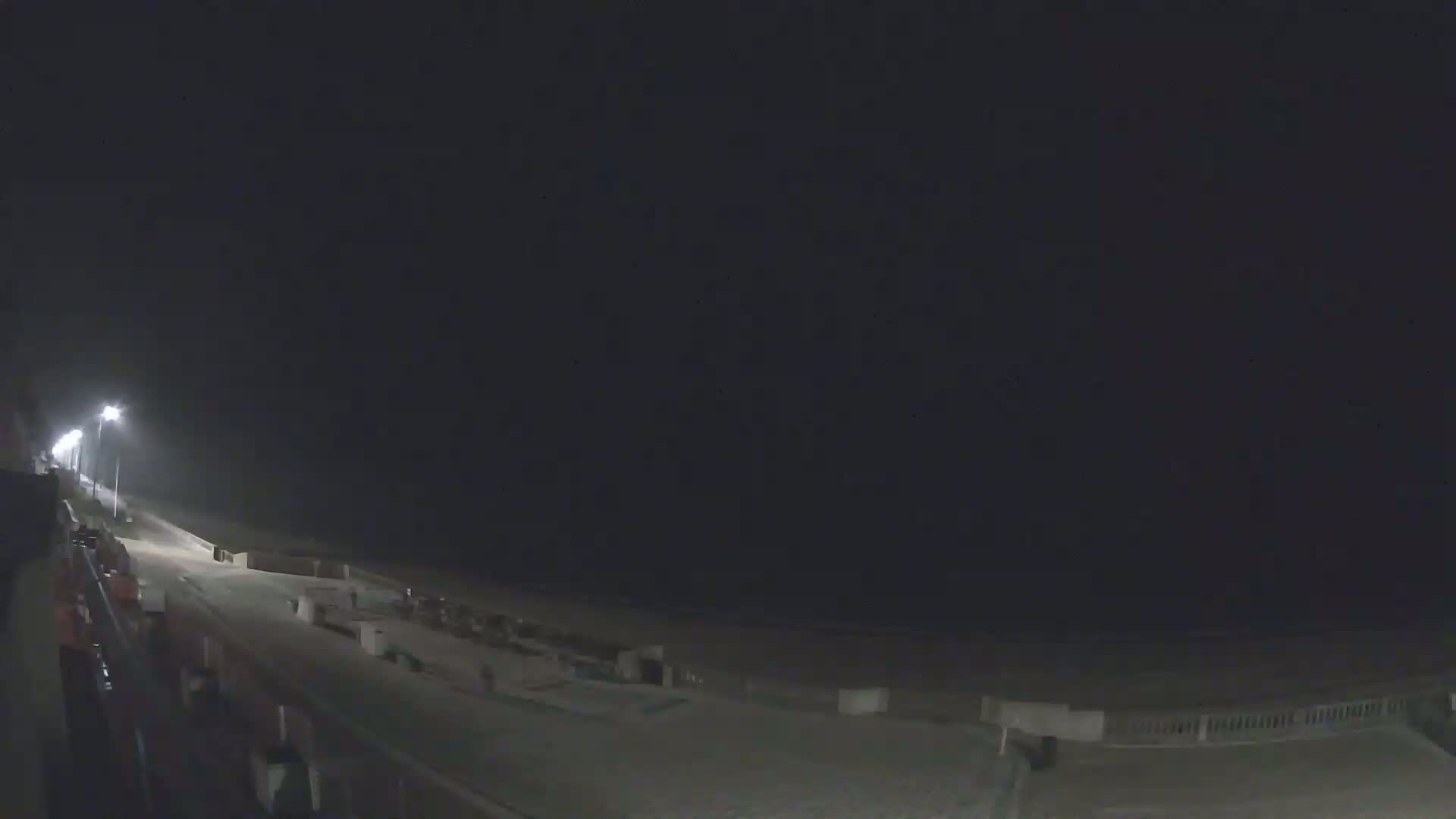 A nighttime view of a dimly lit beach boardwalk and sandy shoreline under a dark sky.