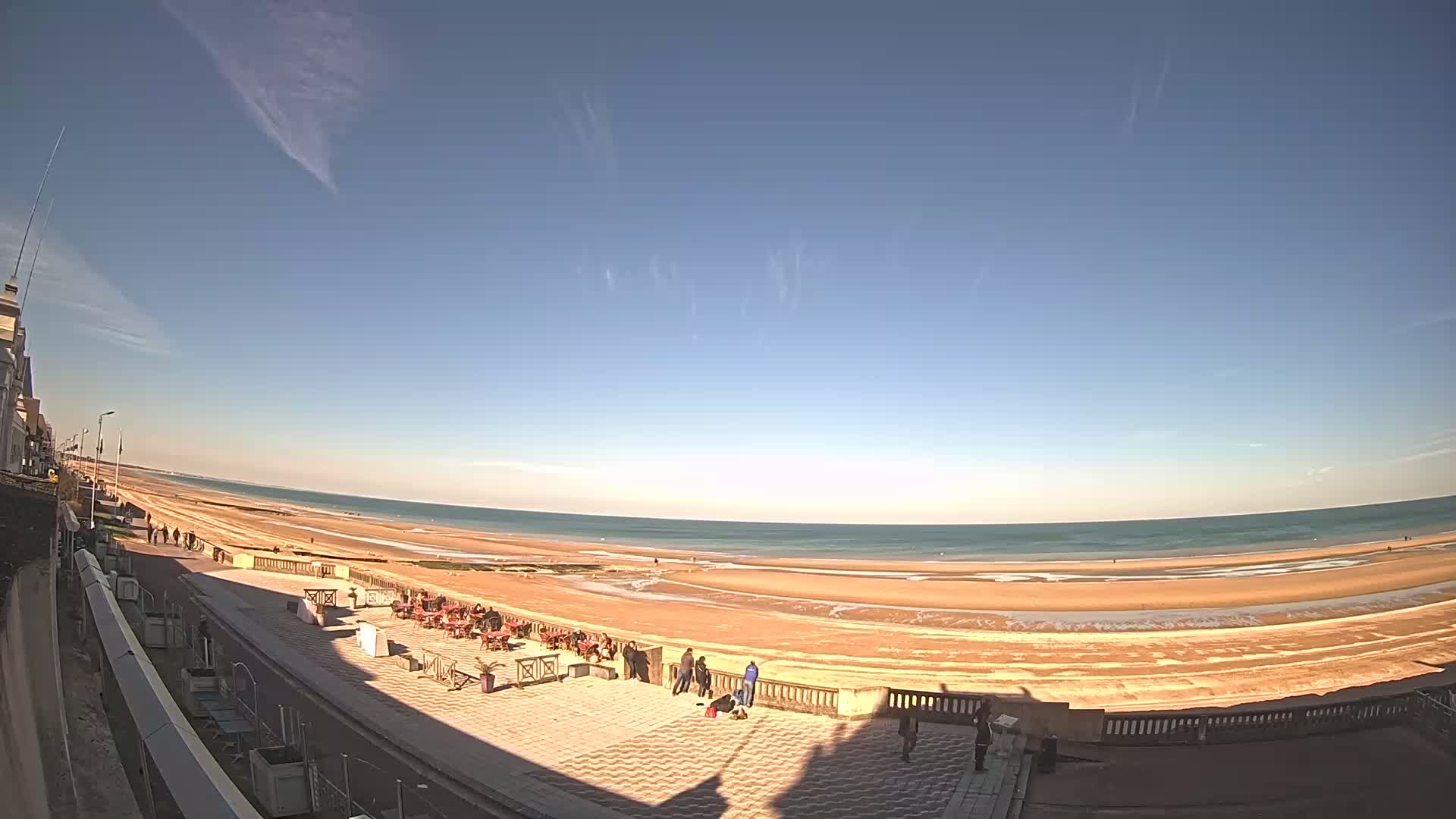 A wide, sandy beach stretches along a calm ocean under a clear blue sky with a few wispy clouds.