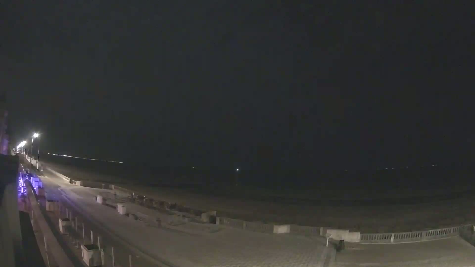 A nighttime view of a snow-covered beach boardwalk and shoreline under a dark sky.