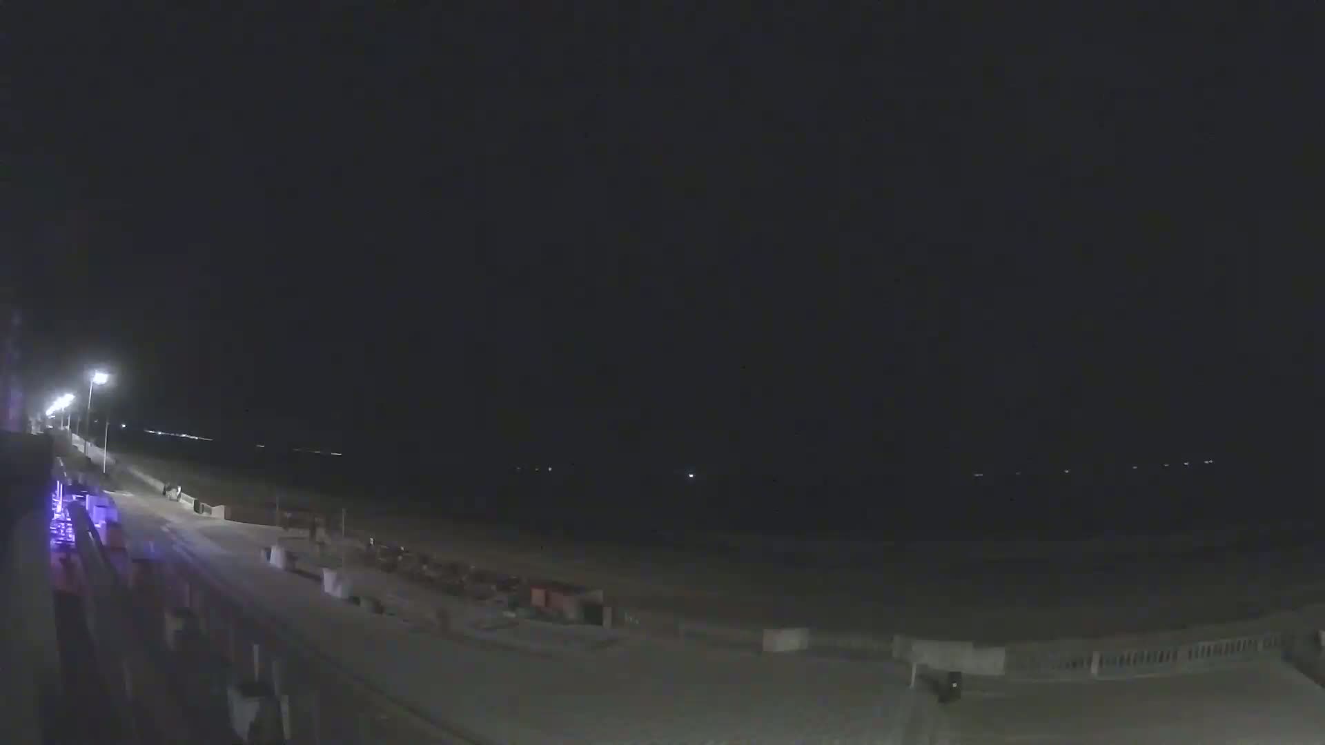 A dark nighttime beach scene is visible with a paved walkway and some structures, illuminated by streetlights.