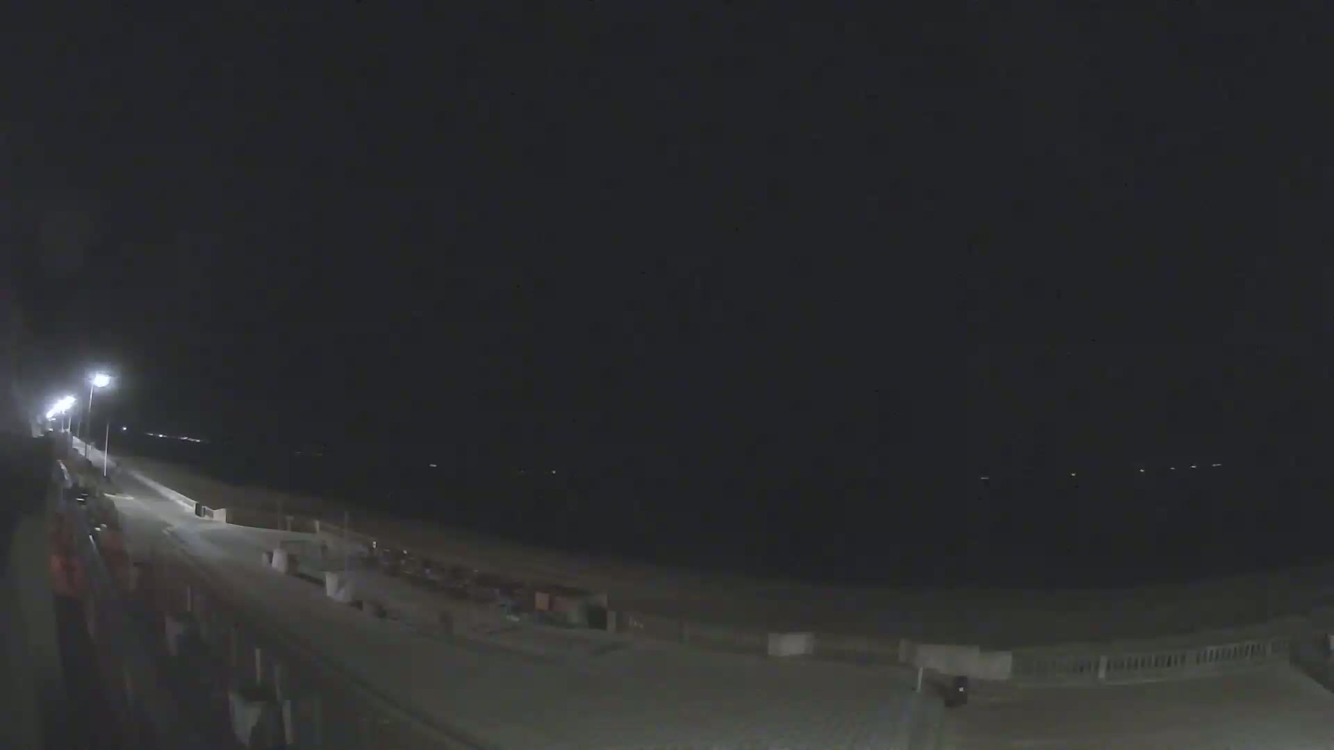 A nighttime view of a beach boardwalk extending to a dark ocean under a clear, dark sky.
