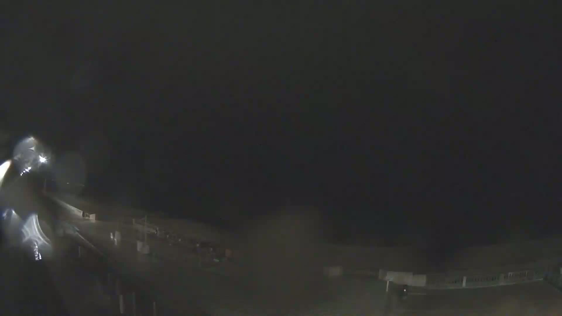 A nighttime, rain-soaked scene shows a road and indistinct structures under a dark sky.