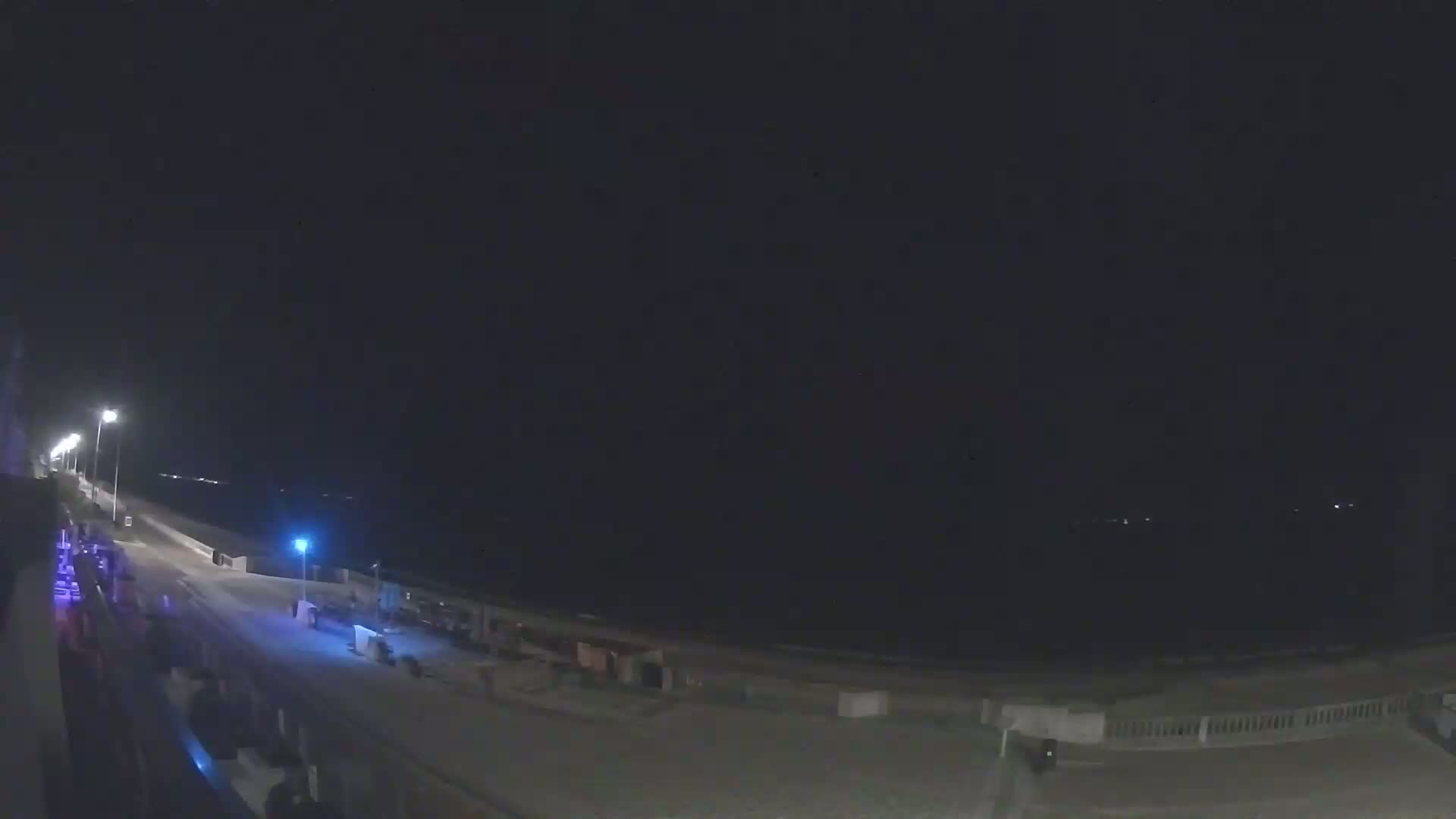 A nighttime view of a mostly empty beach promenade with a dark, clear sky and a calm ocean.