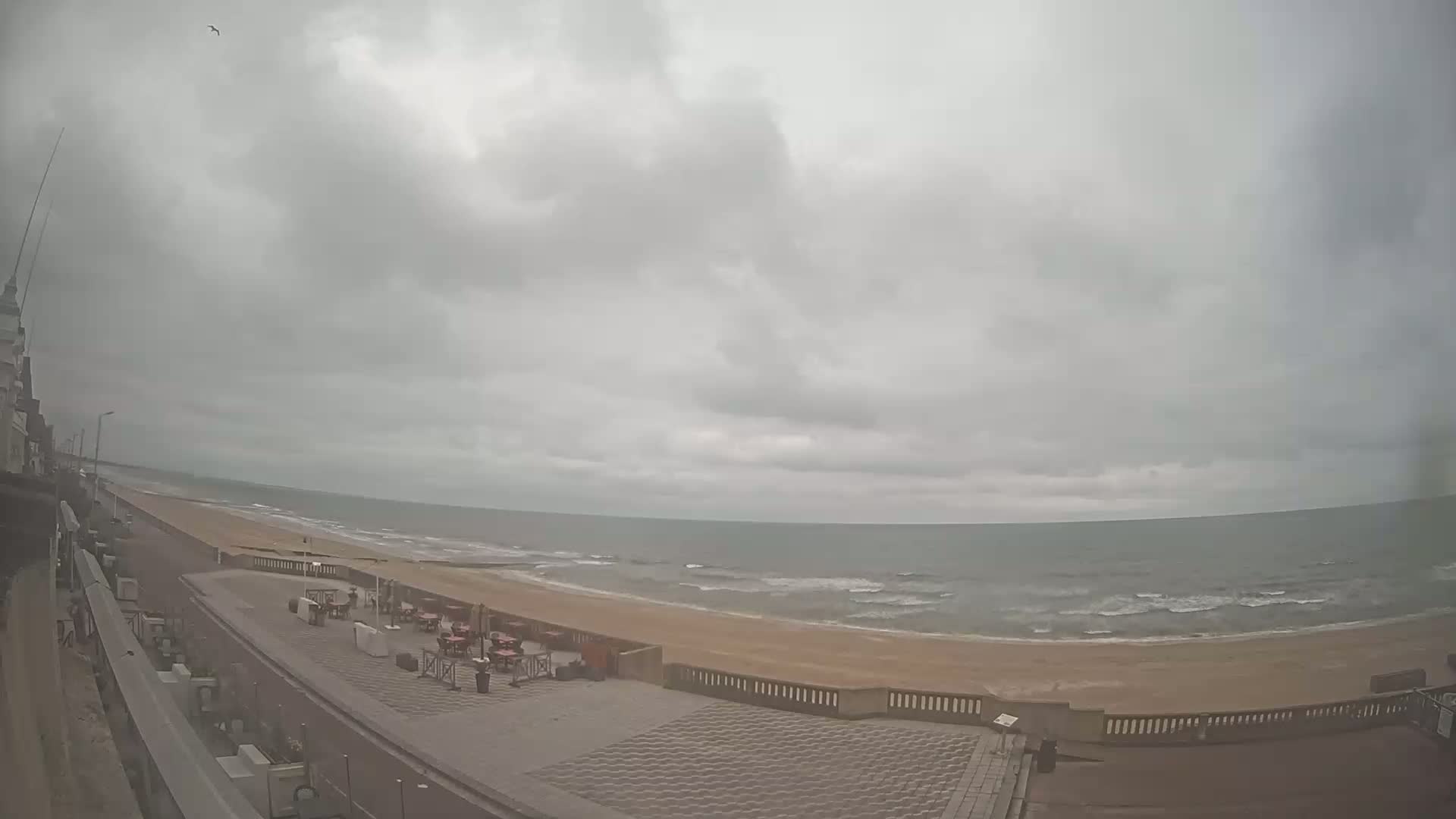 A paved beachfront promenade overlooks a sandy beach and a somewhat choppy sea under an overcast sky.