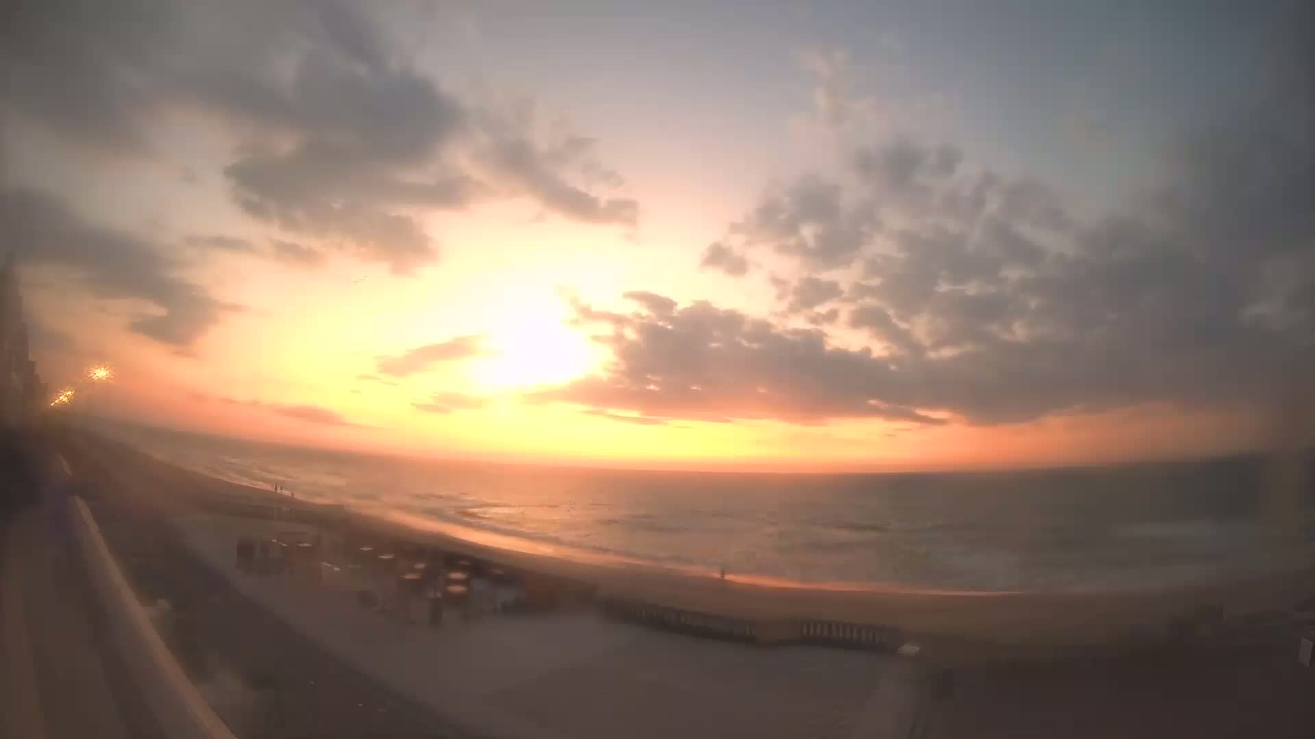 A sunrise over a calm ocean beach, with a few clouds in the sky.