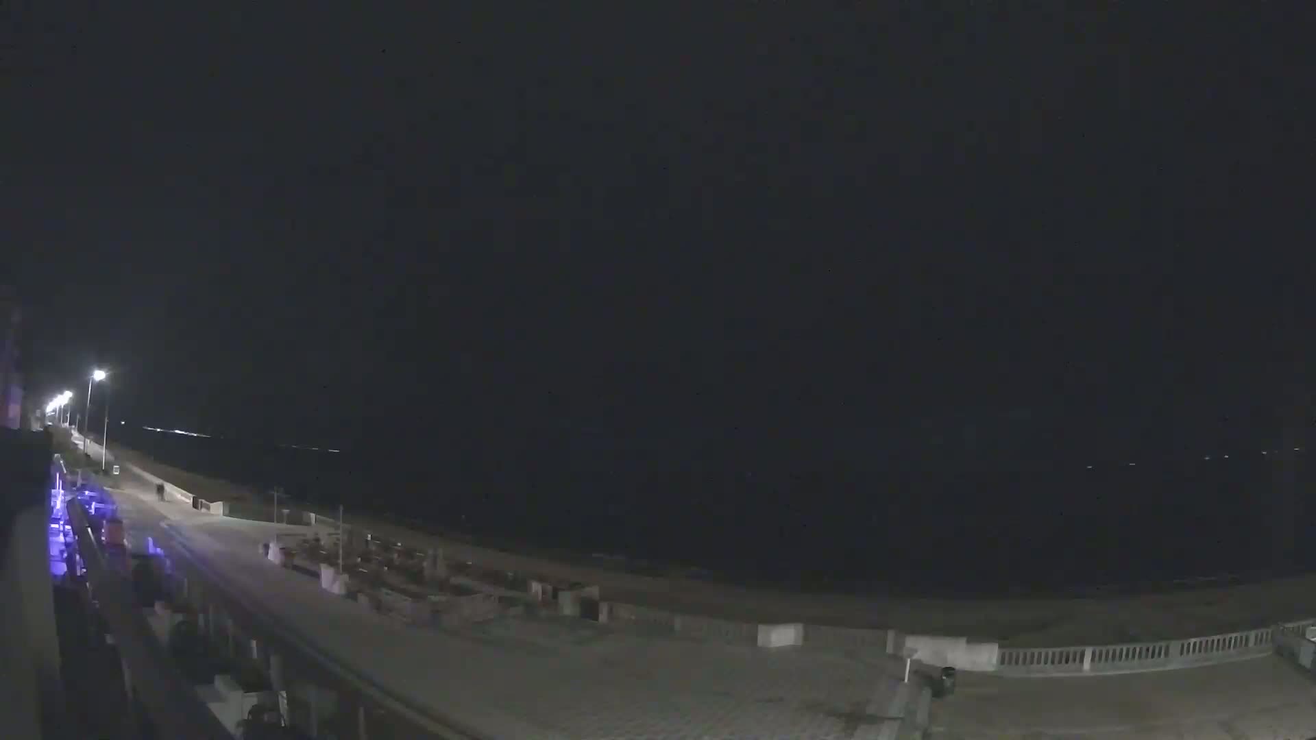 A nighttime view of a beachside promenade and ocean under a dark, clear sky.