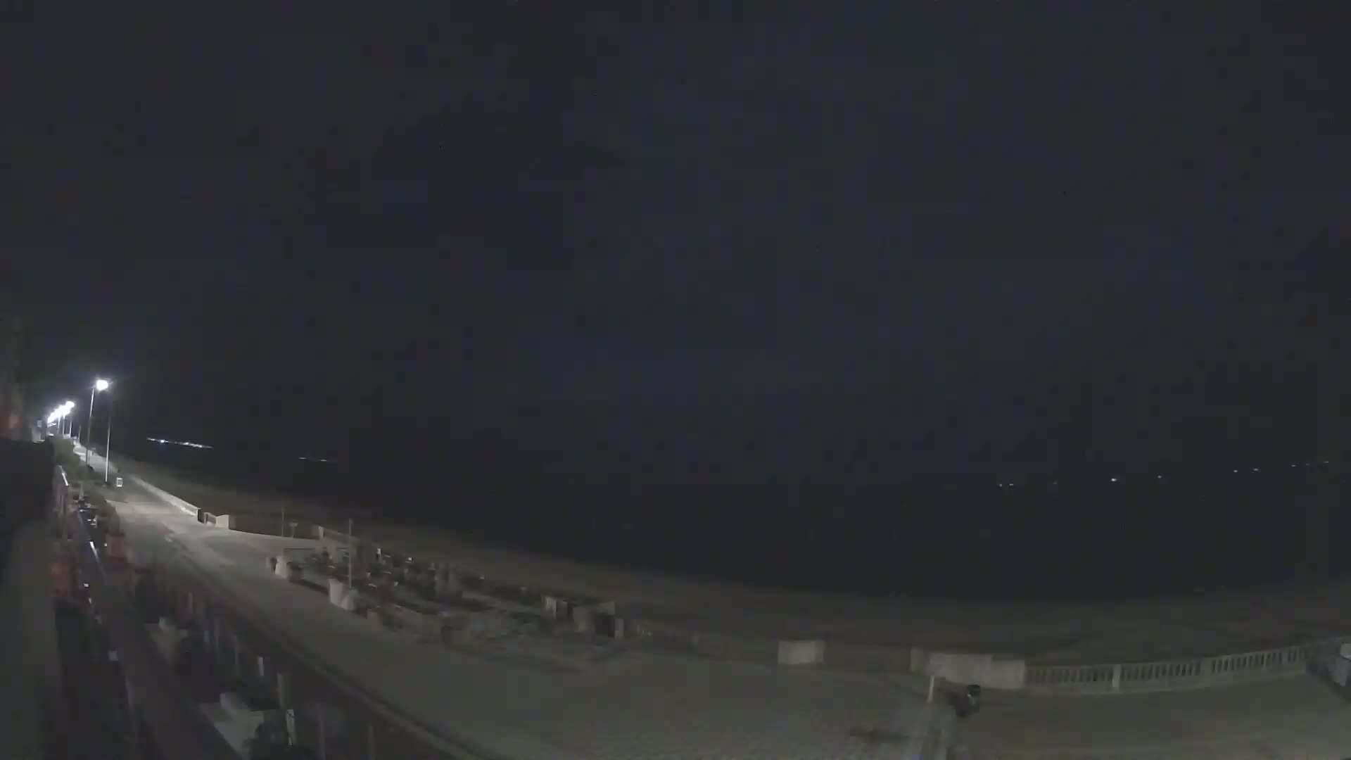 A nighttime view of a mostly empty beach and boardwalk, under a dark sky.