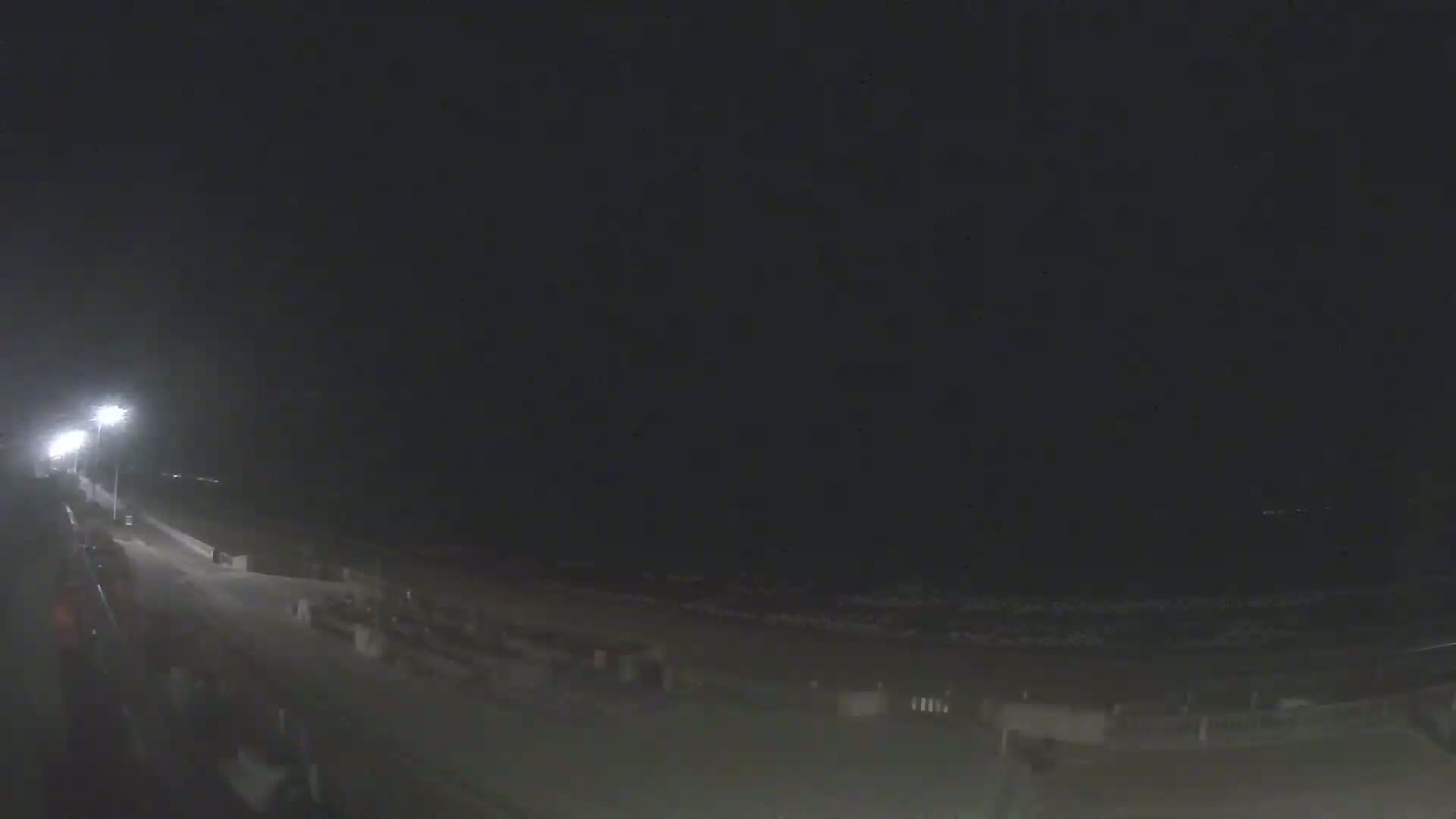 A nighttime view of a beach with a road and some structures visible under a dark sky.