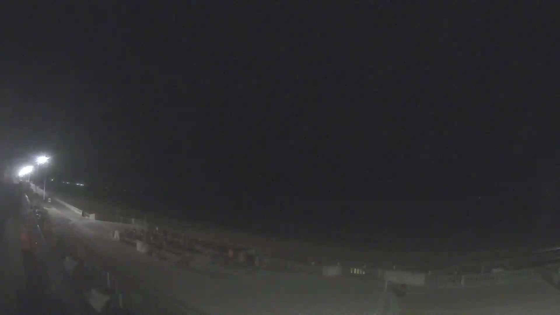 A nighttime view of a dimly lit beach boardwalk with a few people visible.