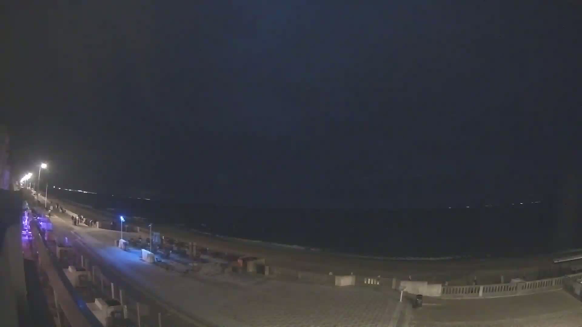A nighttime view of a beach boardwalk with a dark, overcast sky and a calm ocean.
