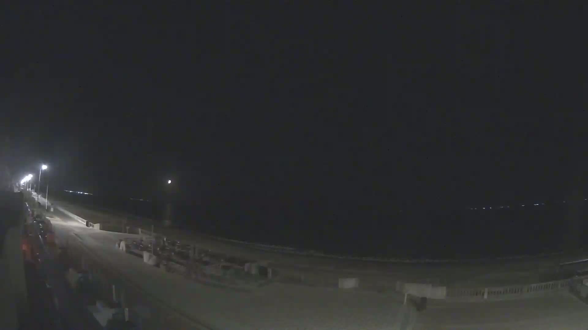 A nighttime view of a beach with a boardwalk and streetlights, under a dark sky.
