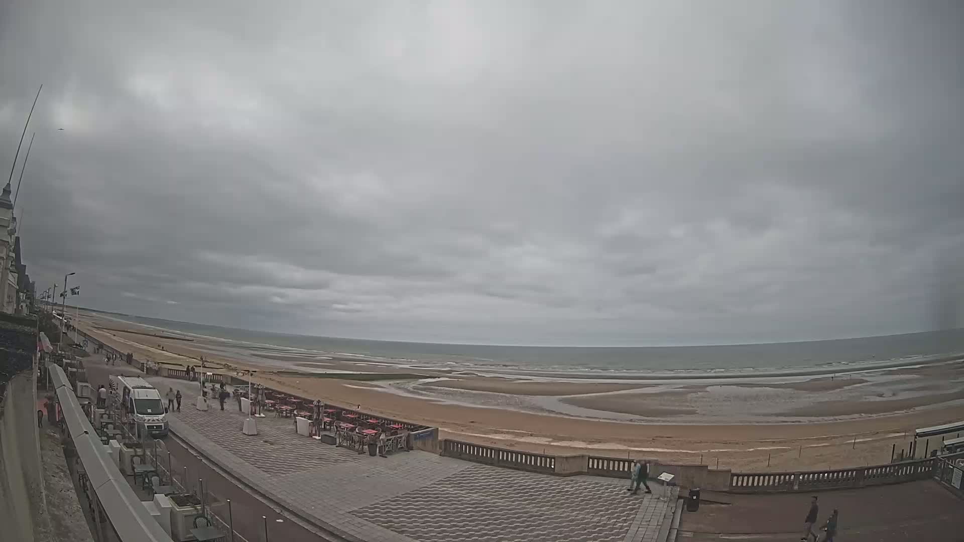 A wide shot of a beachside promenade on an overcast day, showing a mostly sandy beach with some exposed tidal flats and a calm sea.