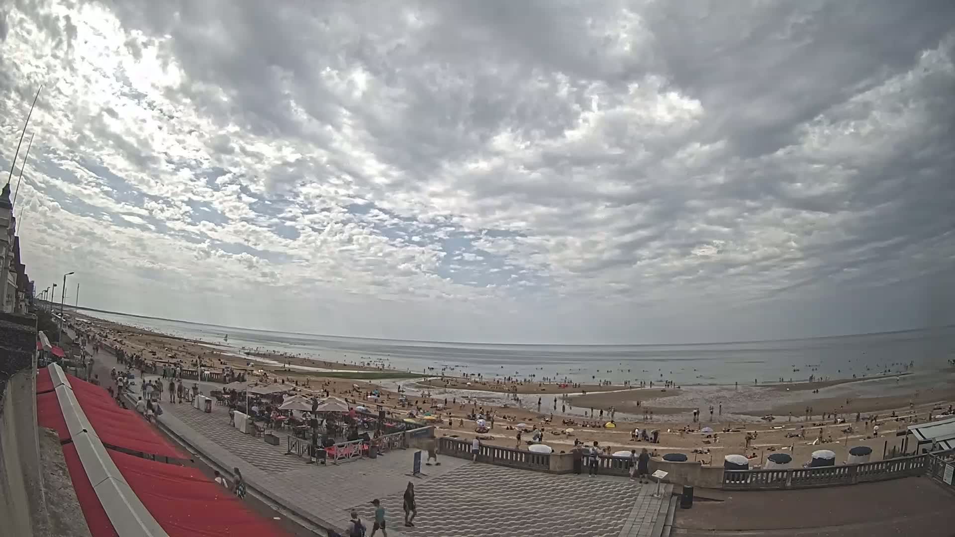 A crowded beach with people sunbathing and swimming under a partly cloudy sky.