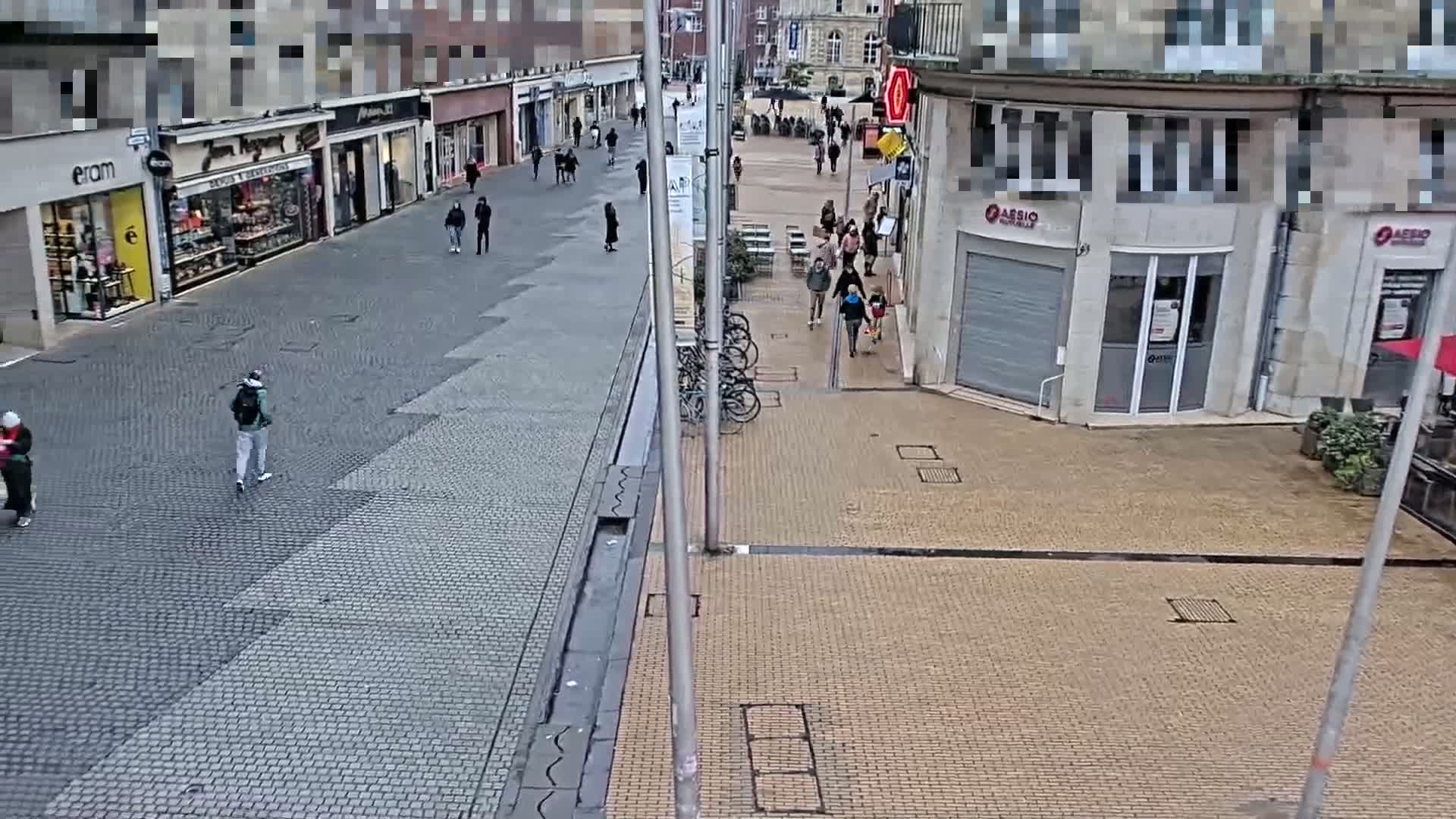 A mostly empty cobblestone pedestrian street with several people walking, some shops, and several bicycles leaning against a rack.
