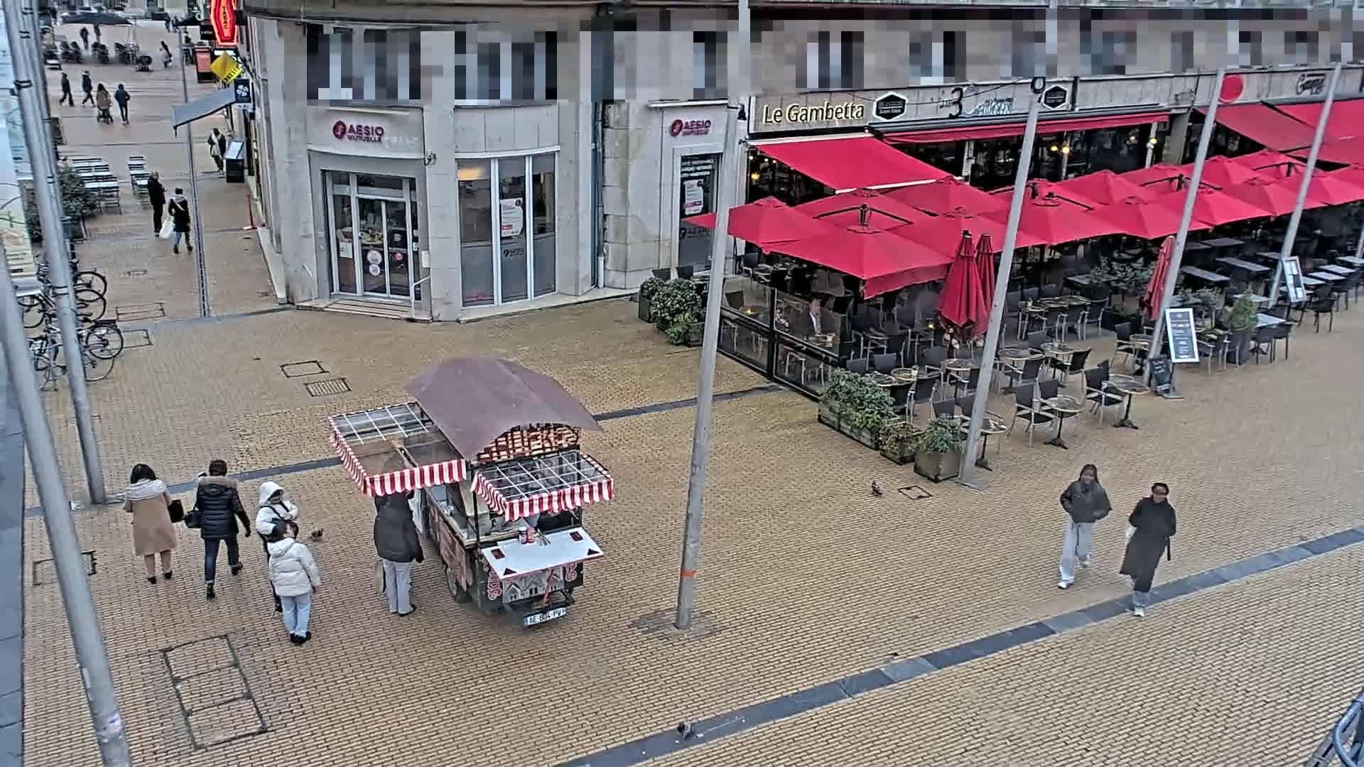 A street scene shows a food cart, pedestrians, and an outdoor cafe with red umbrellas under an overcast sky.