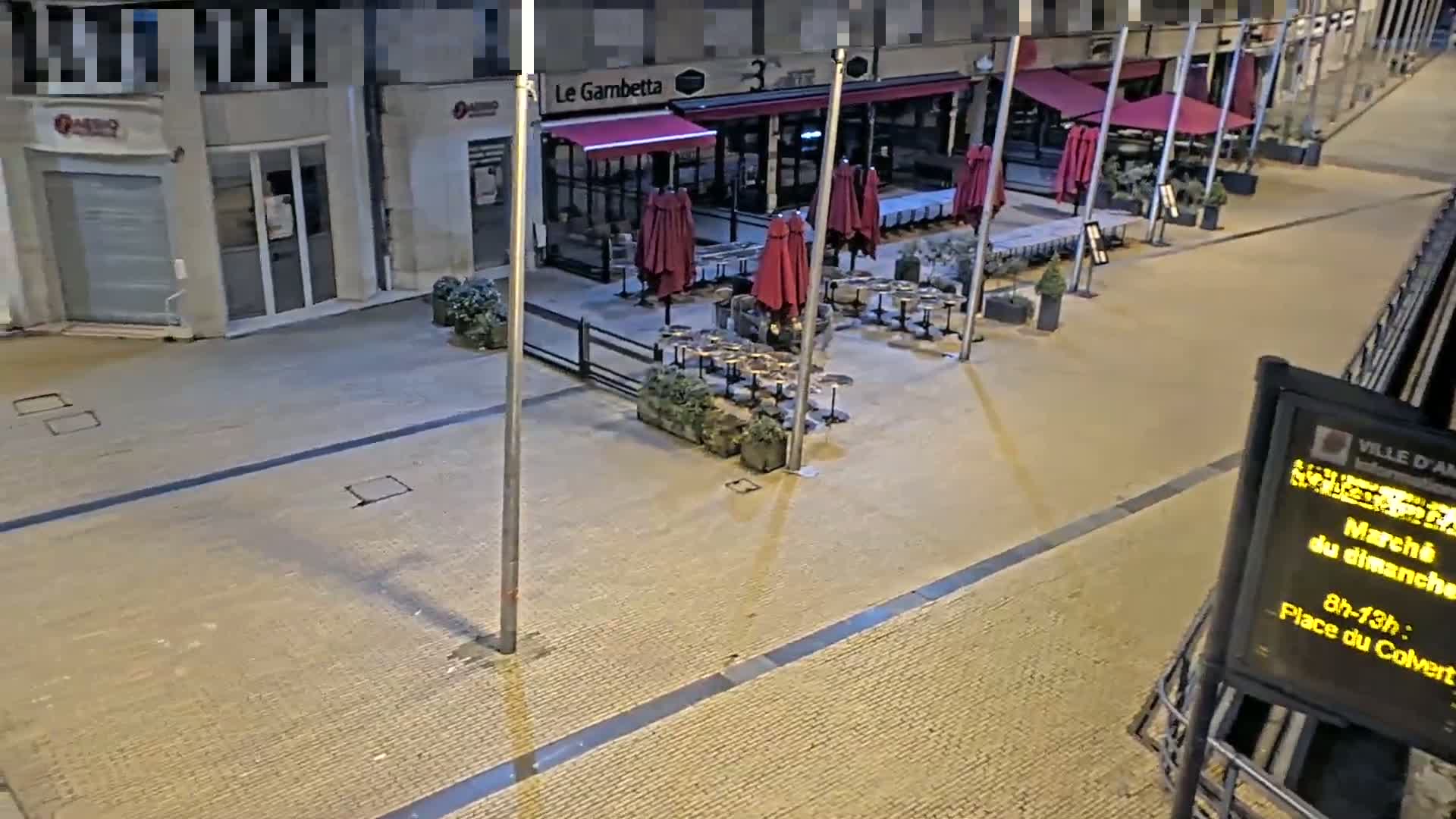 An empty outdoor cafe with maroon umbrellas and dark tables sits on a paved street at night.