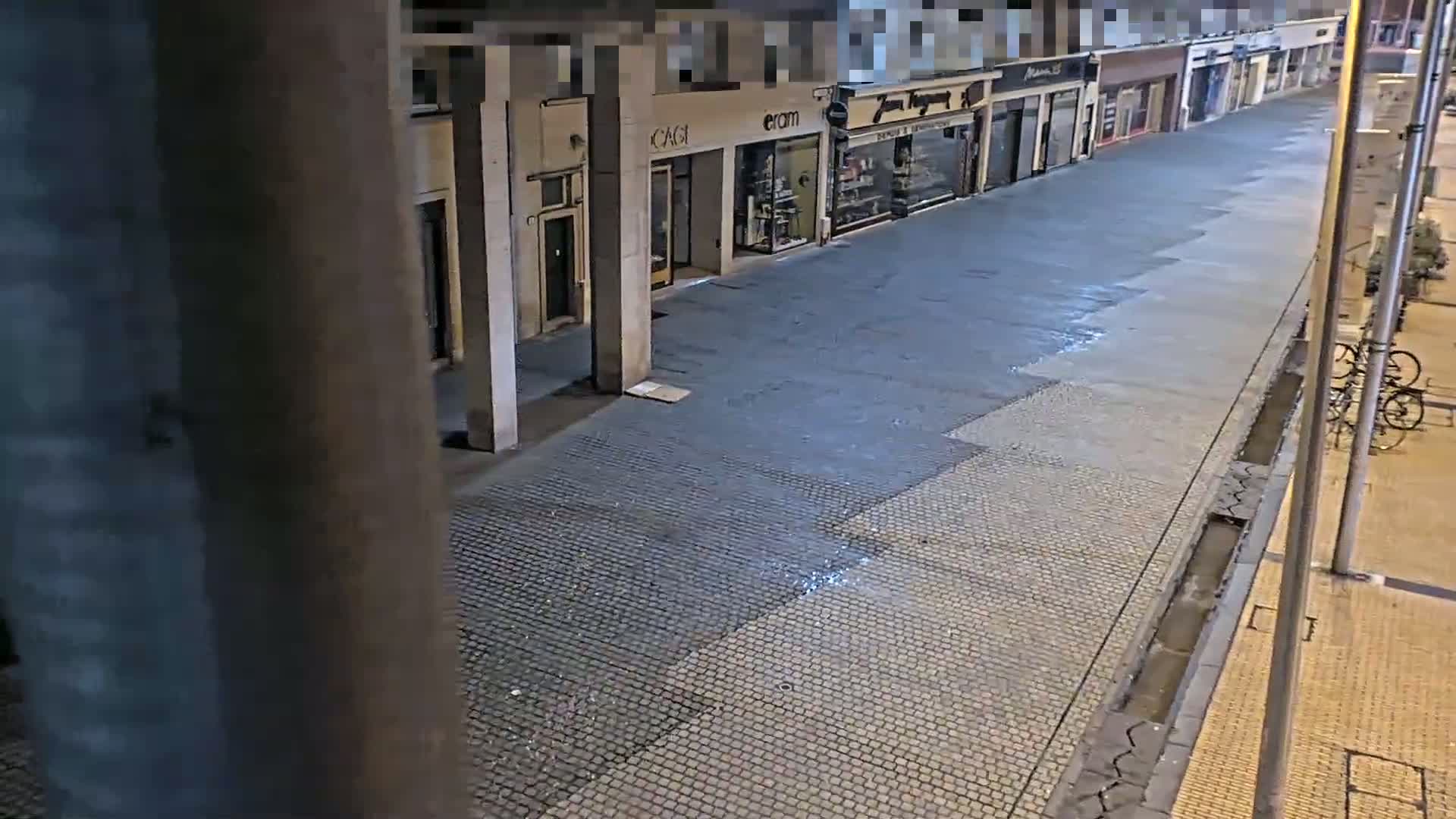 A wet, empty city street at night is lined with closed shops.