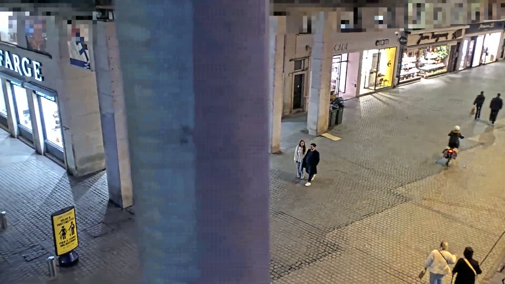 A high-angle, nighttime view of a cobblestone street with several pedestrians and storefronts.