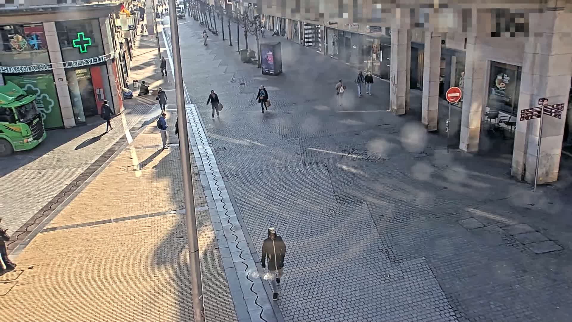 A mostly empty cobblestone street with a few pedestrians and a green truck parked nearby on a slightly hazy day.