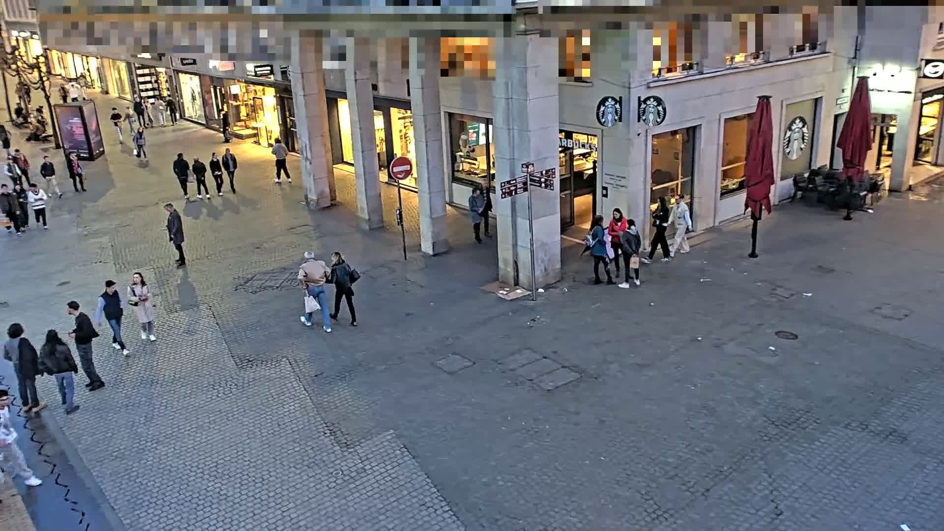 A high-angle view shows a city street scene at dusk with several people walking around a Starbucks and several storefronts.