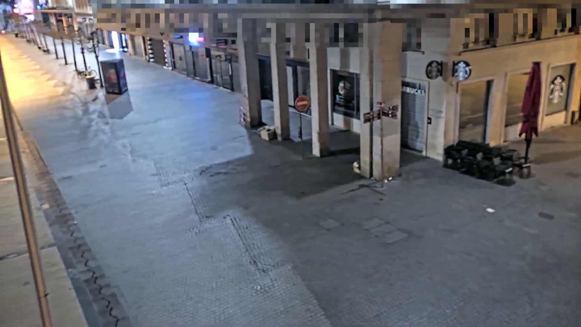A mostly empty, paved city street at night, with a few buildings and a closed Starbucks visible.