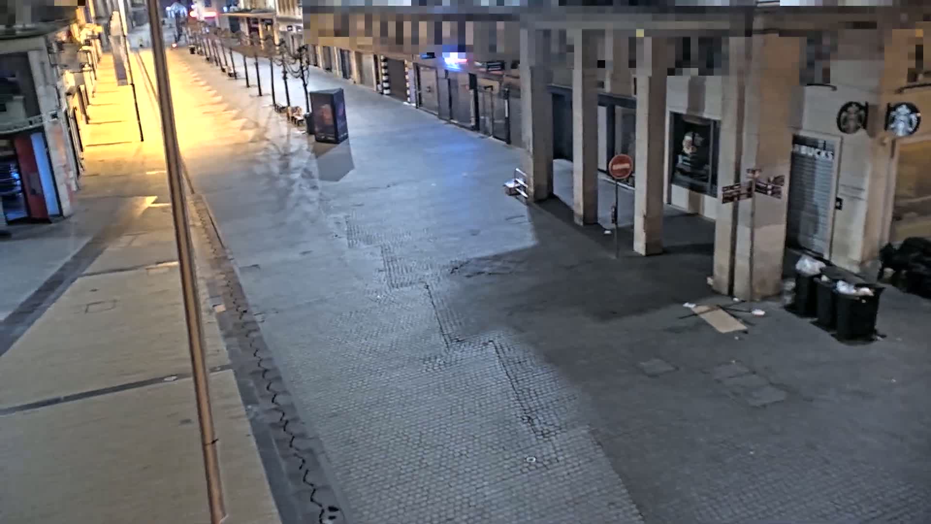 A mostly empty, paved street at night, lined with closed shops and buildings, is dimly lit by streetlights.
