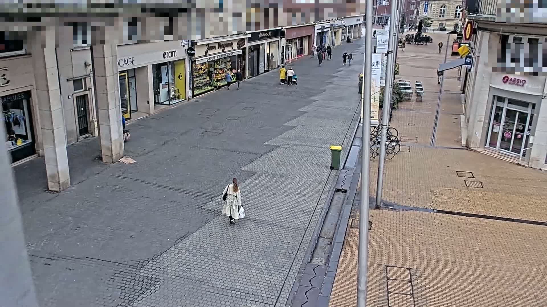 A woman walks down a mostly empty pedestrian street lined with shops on a cloudy day.