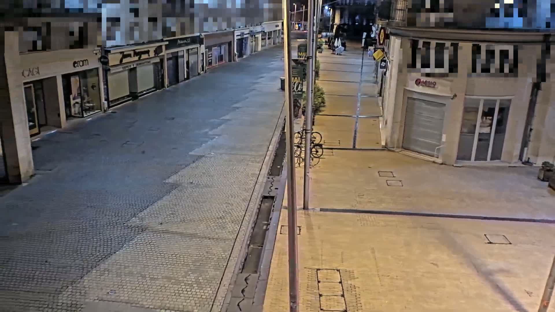 A mostly empty, paved street at night, lined with closed shops, with a few bicycles leaning against a pole.