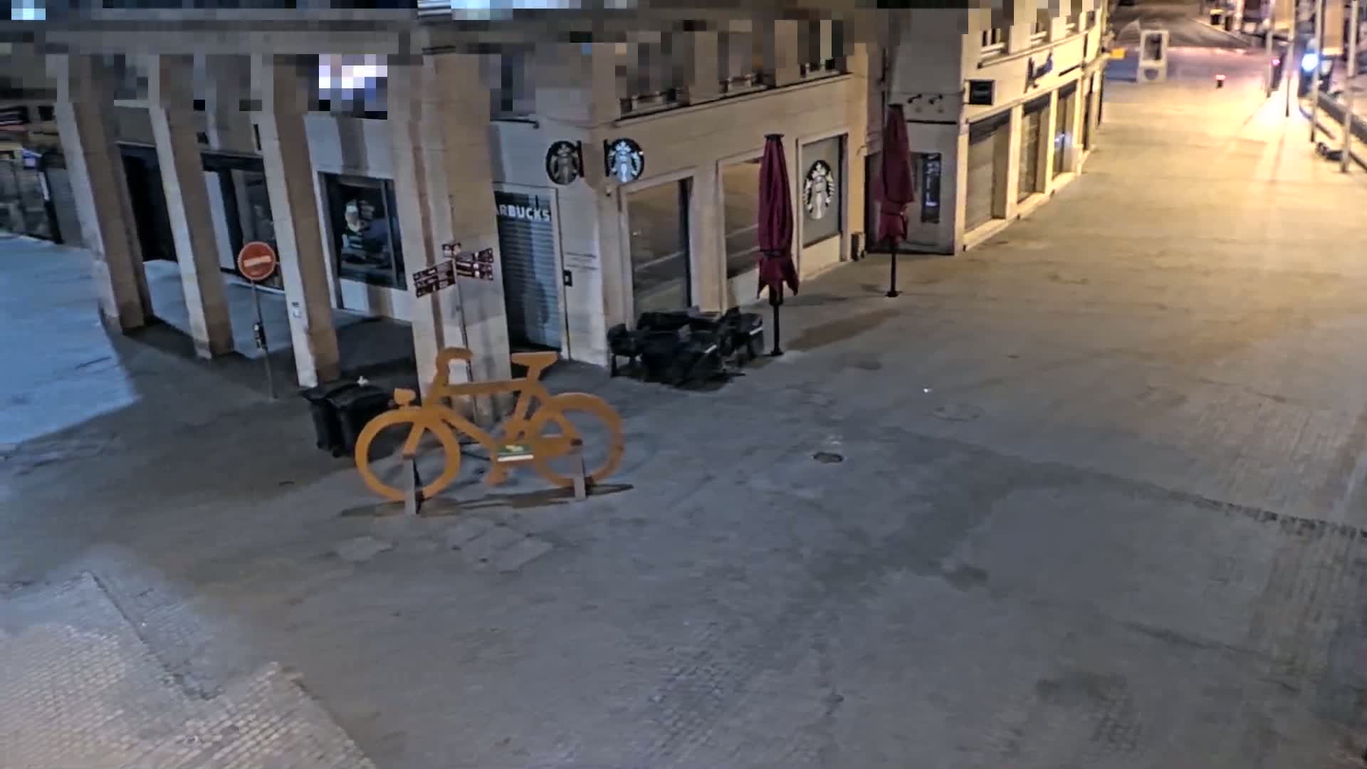 A large, light-brown bicycle sculpture stands outside a Starbucks at night on a mostly empty, paved street.
