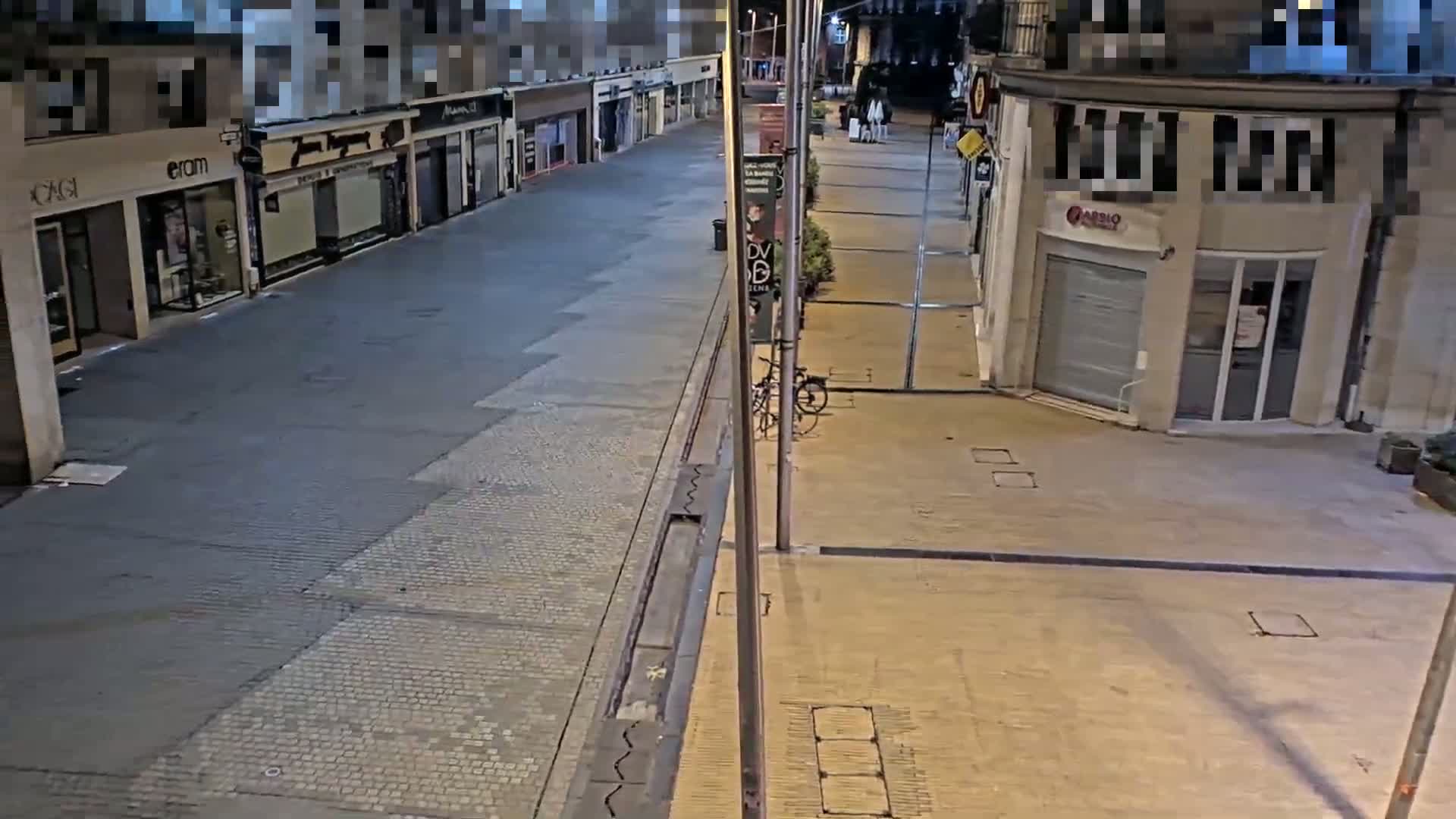 A mostly empty, paved street at night, lined with shops and a bicycle leaning against a lamppost.