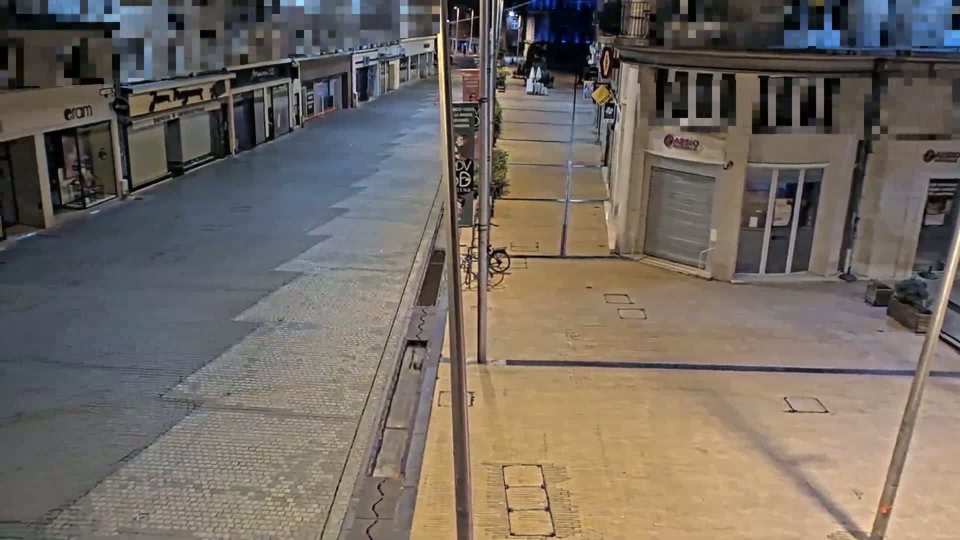 An empty, stone-paved street at night, lined with closed shops and a single bicycle parked near a light post.