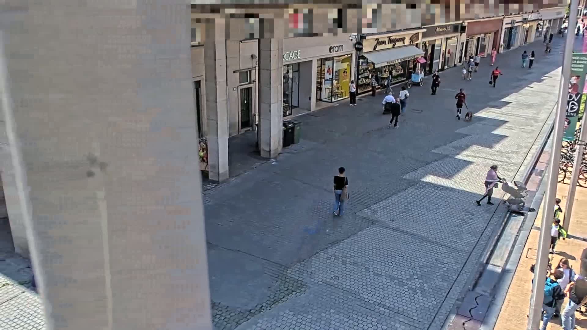 A paved pedestrian area with shops and people walking on a sunny day.