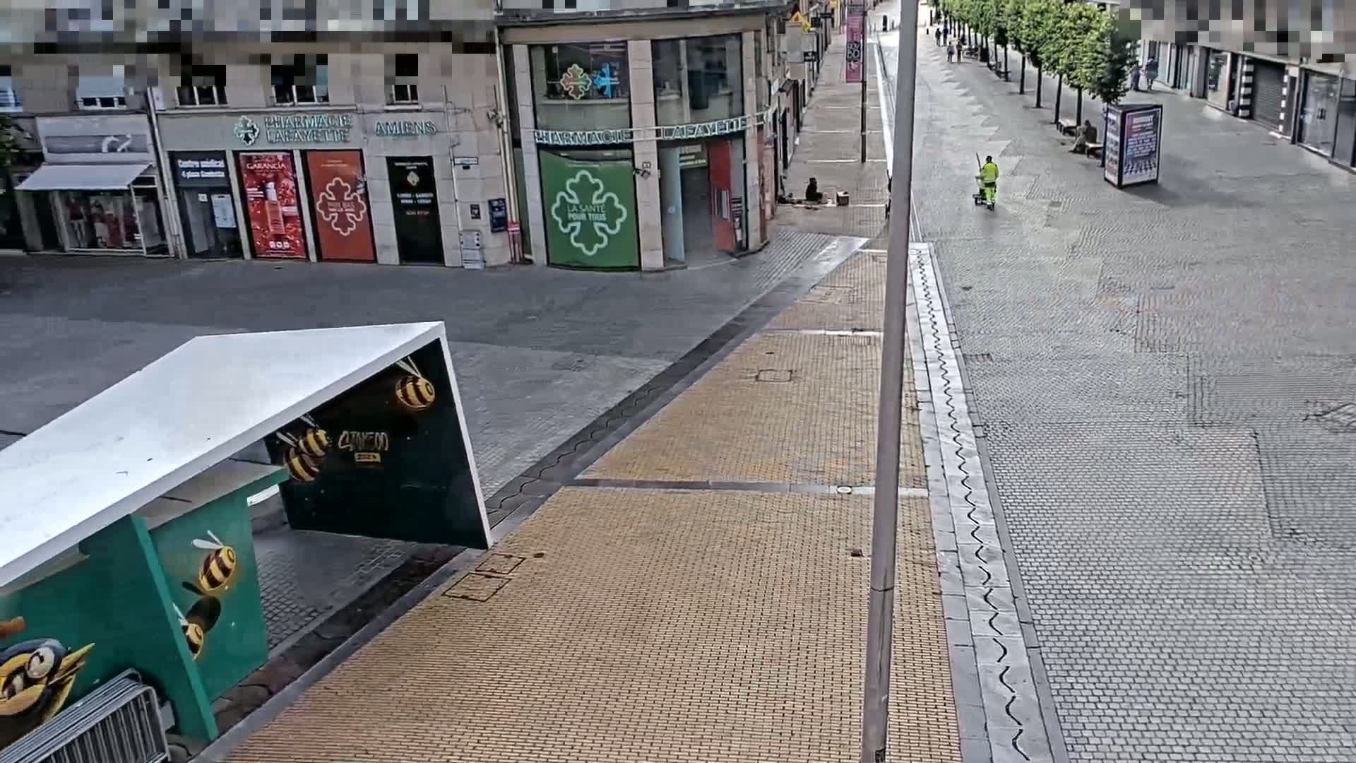 A mostly empty city street with a person sweeping, under a partly cloudy sky.