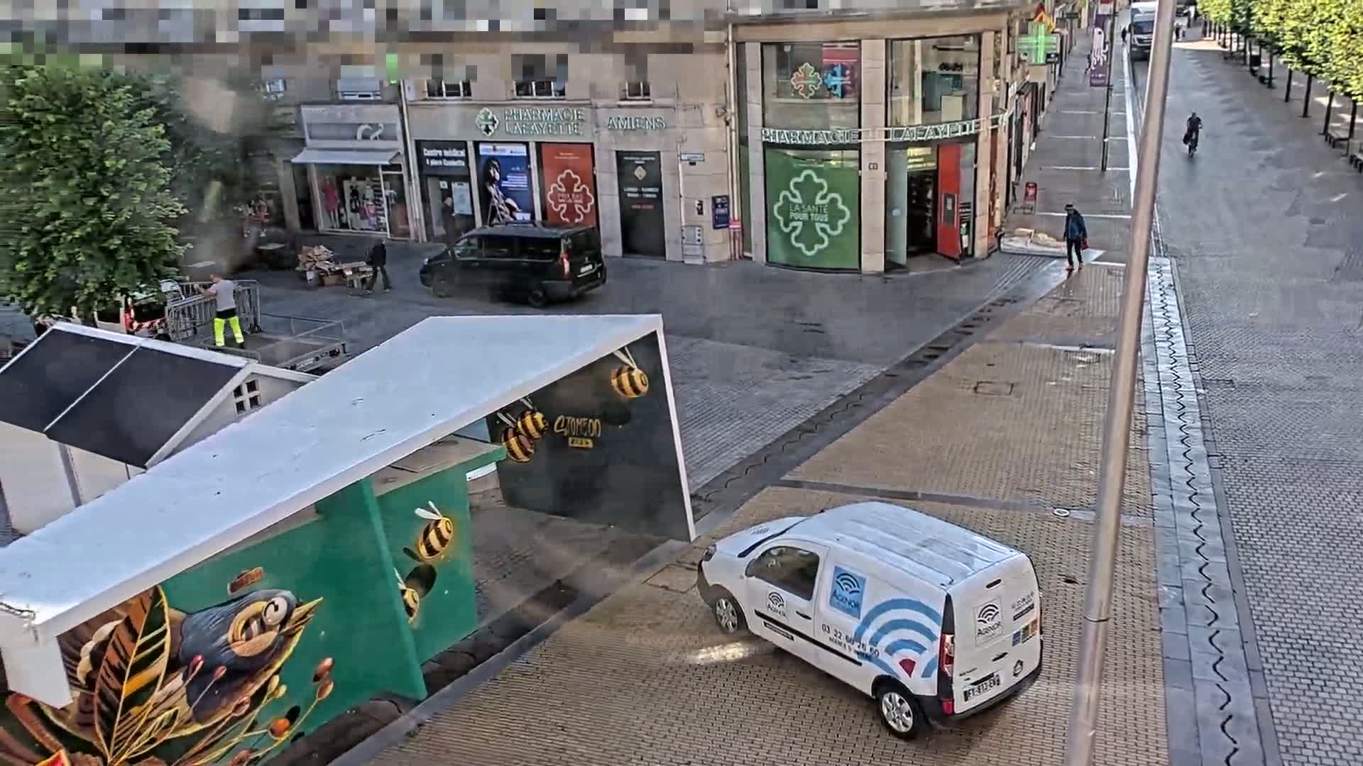 A white van is parked near a building with green and white murals on a sunny day in a paved city square.