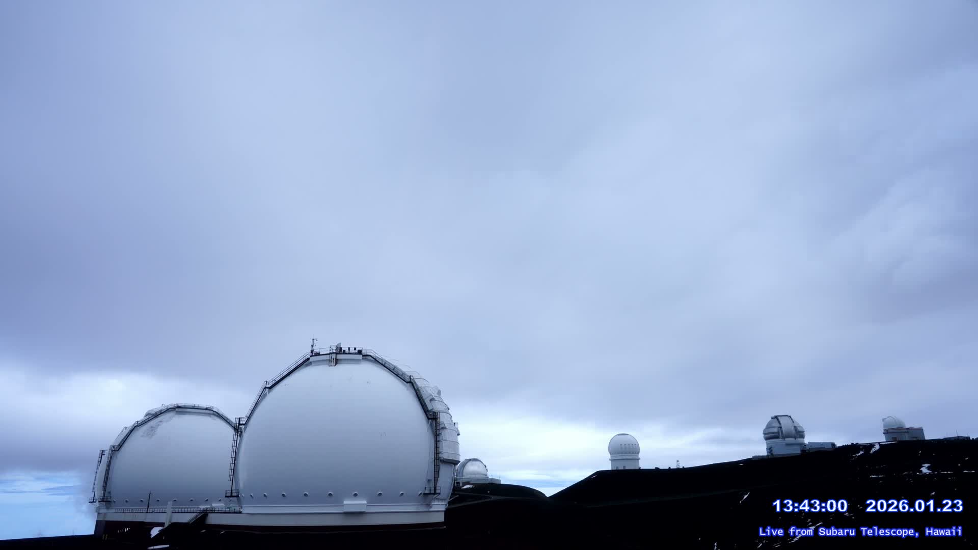 Several white observatory domes are visible on a dark, elevated landscape under a heavily overcast and cloudy sky.