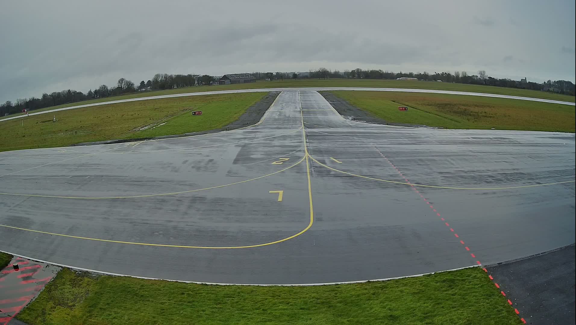 A wet, gray tarmac airport runway and taxiway are visible under an overcast sky.