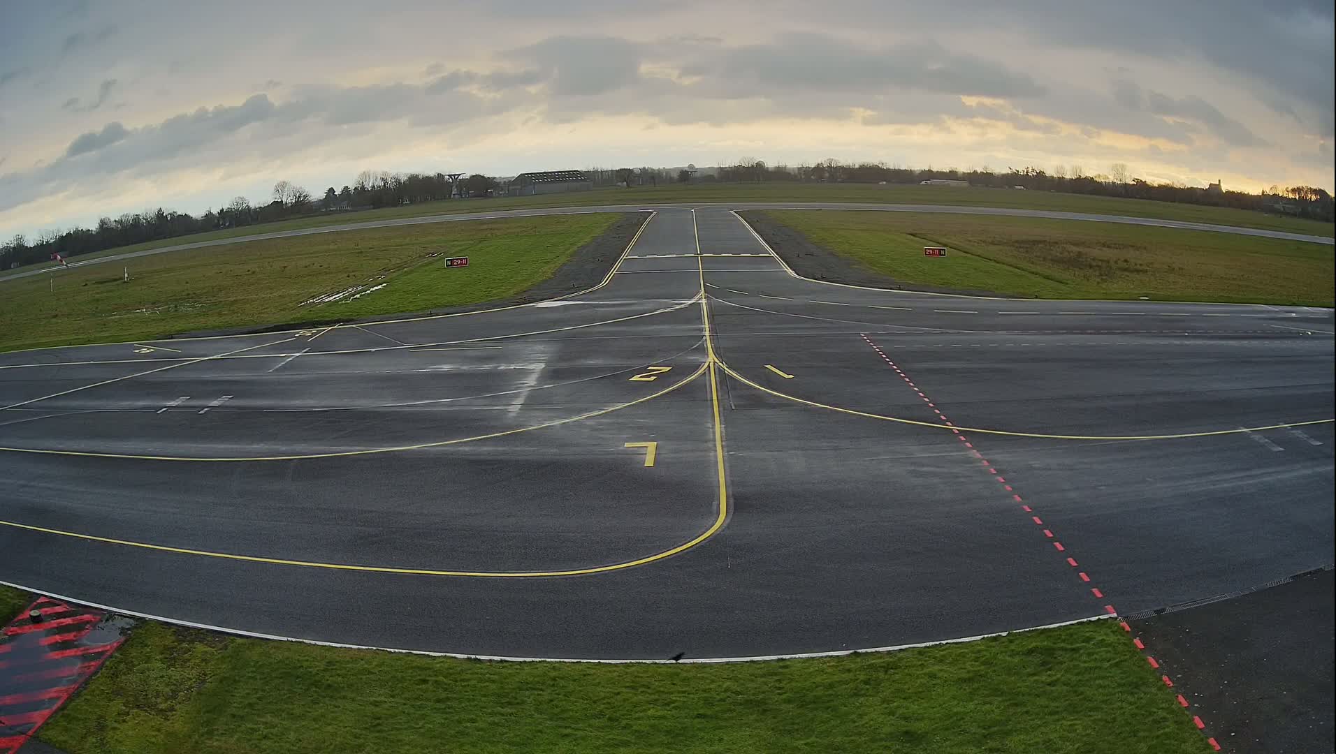 An empty airport tarmac with yellow and red lines under a cloudy sky.