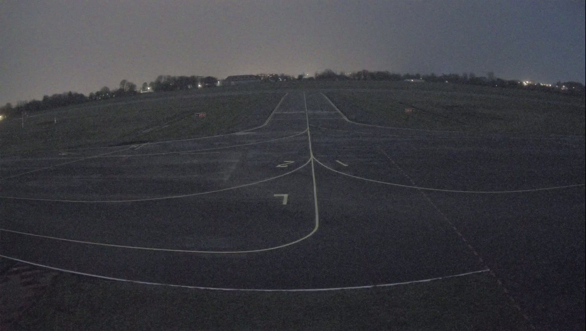 A dark asphalt runway with painted lines extends into the distance under a dusky sky.