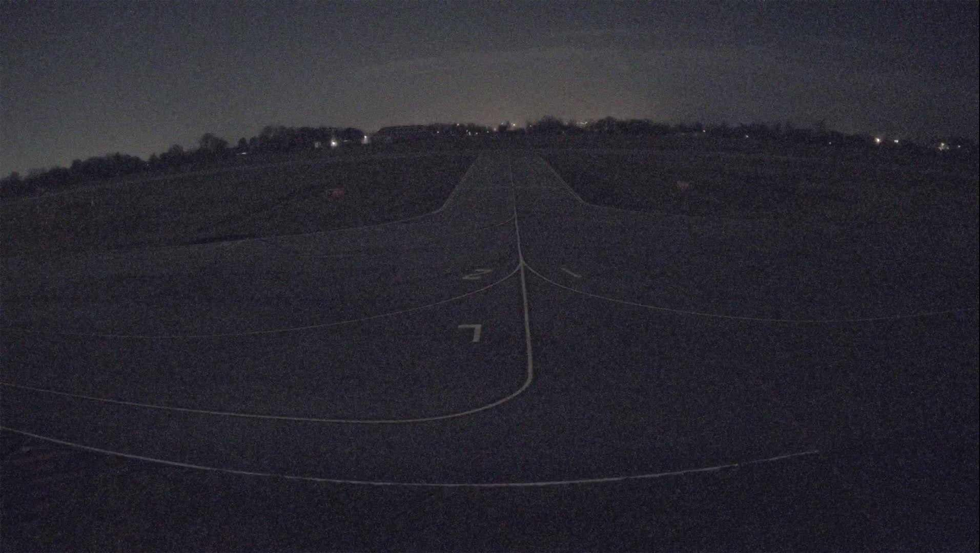 A dark asphalt runway with painted markings is visible at night under a cloudy sky.