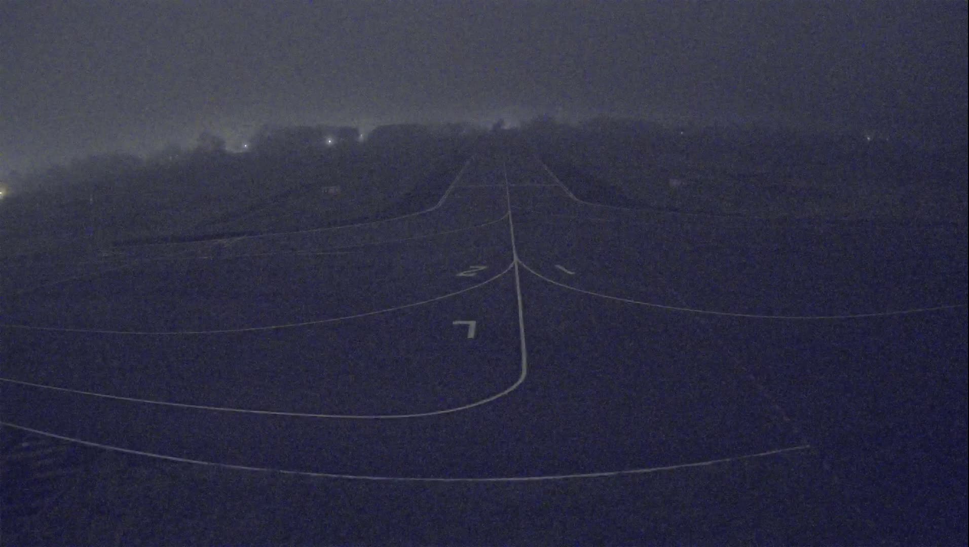 A foggy night scene shows a dark asphalt runway with white lane markings.