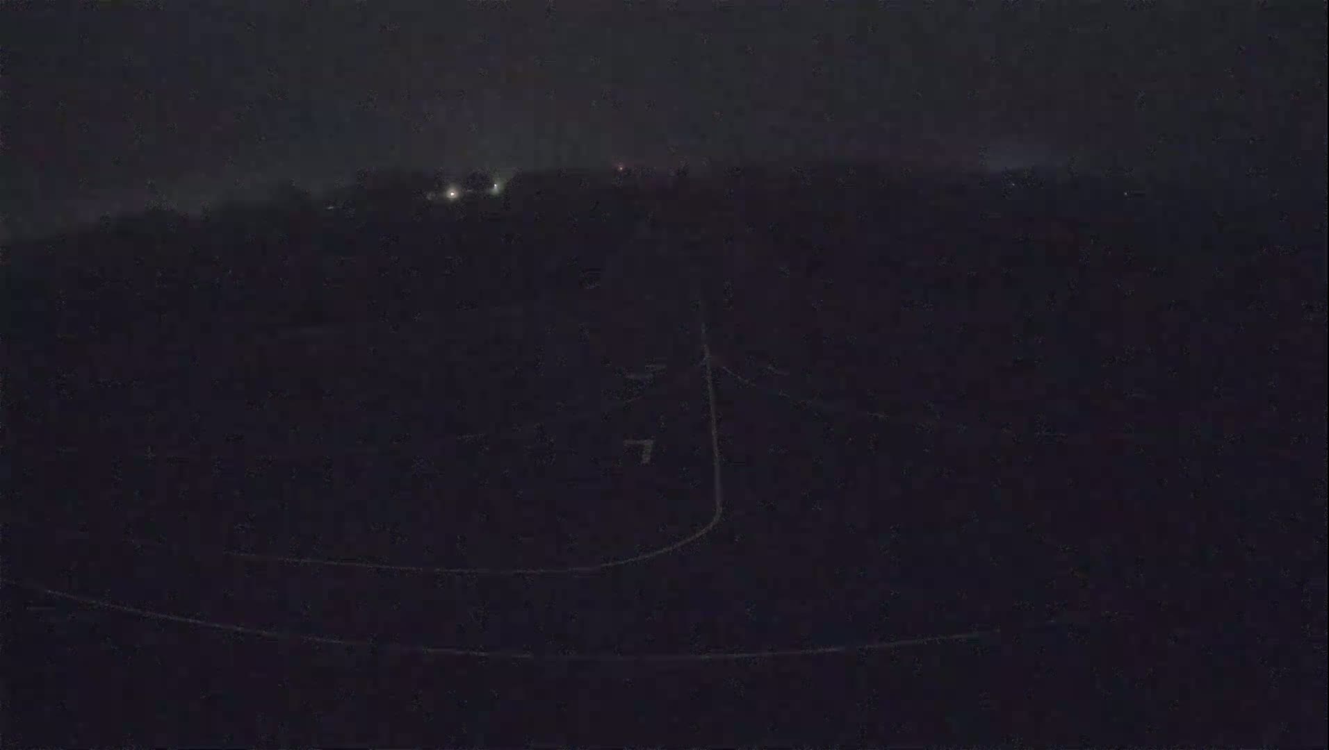 A dark, nighttime scene shows a dimly lit road curving through a field under a foggy sky.