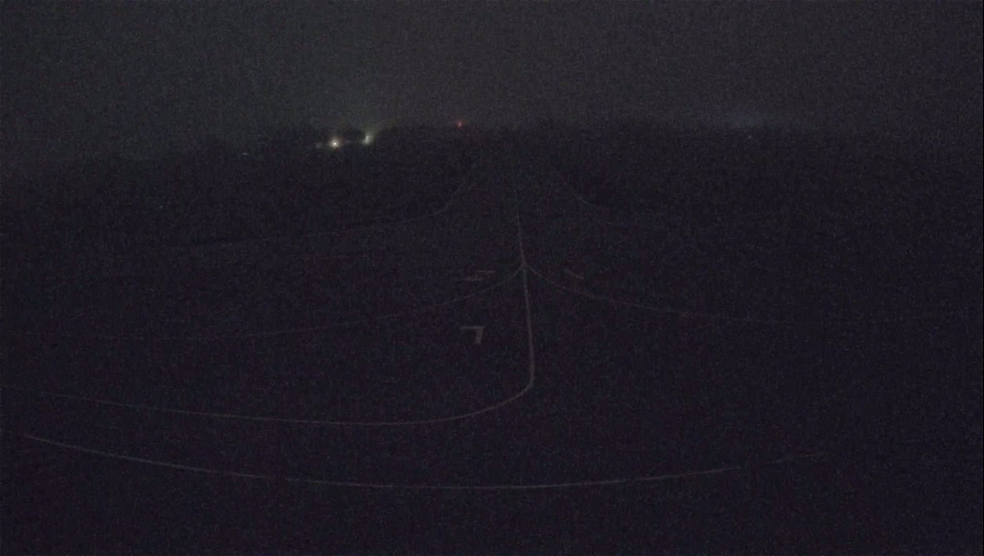 A dark, foggy nighttime scene shows faintly illuminated roadways and distant lights.