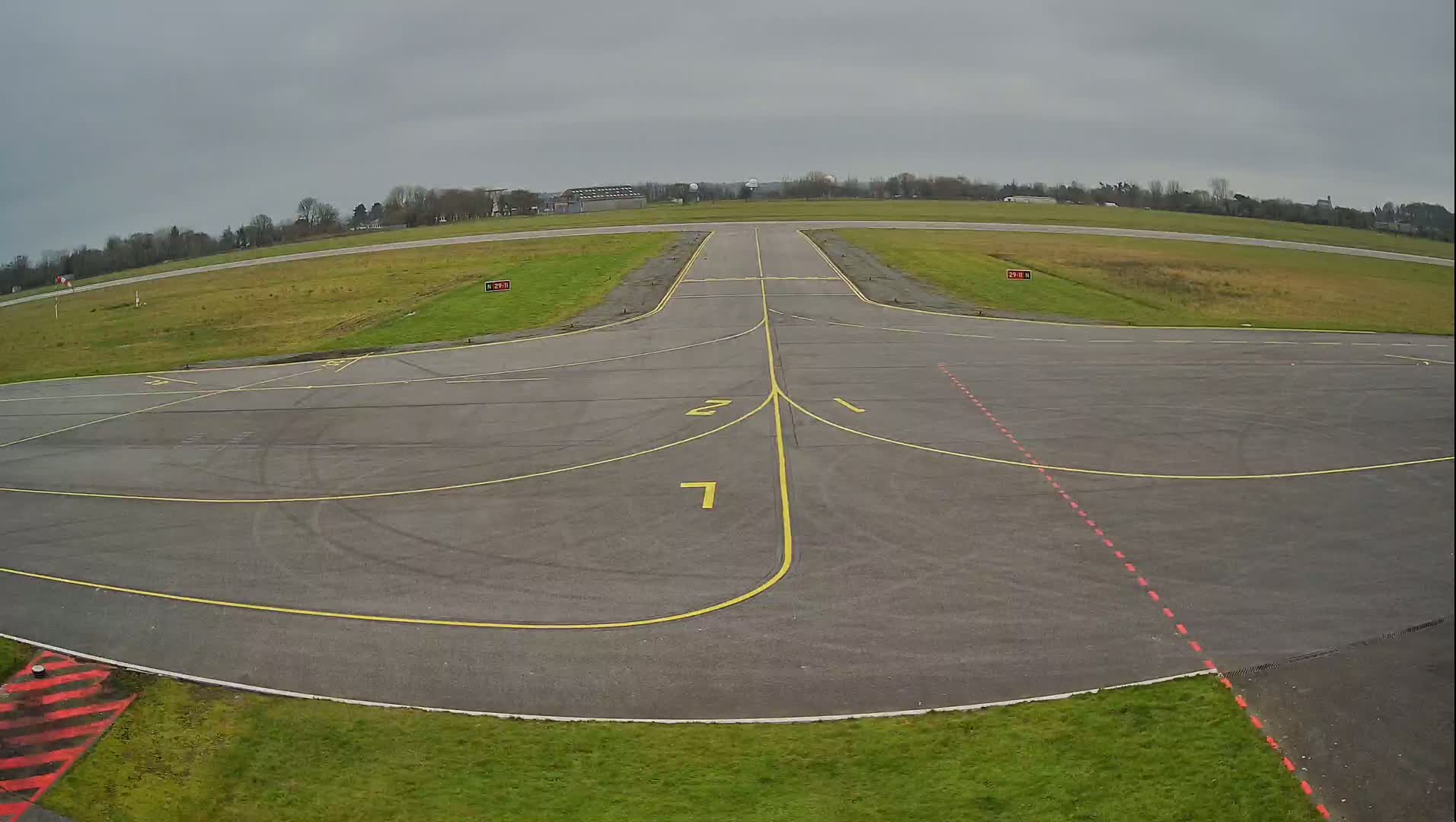 An empty airport tarmac with yellow and red markings is visible under an overcast sky.