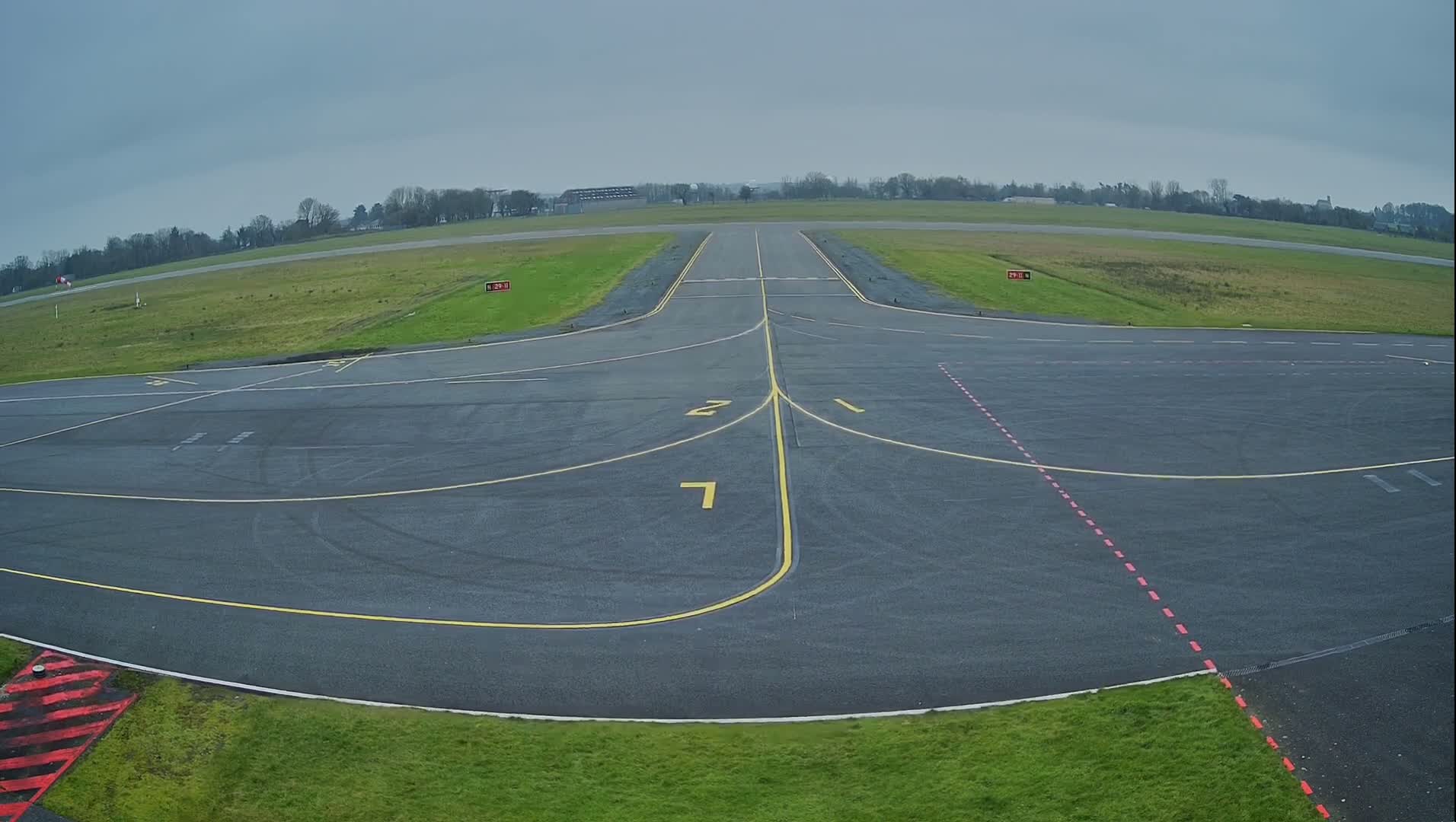 A runway and taxiway at a small airport on an overcast day.