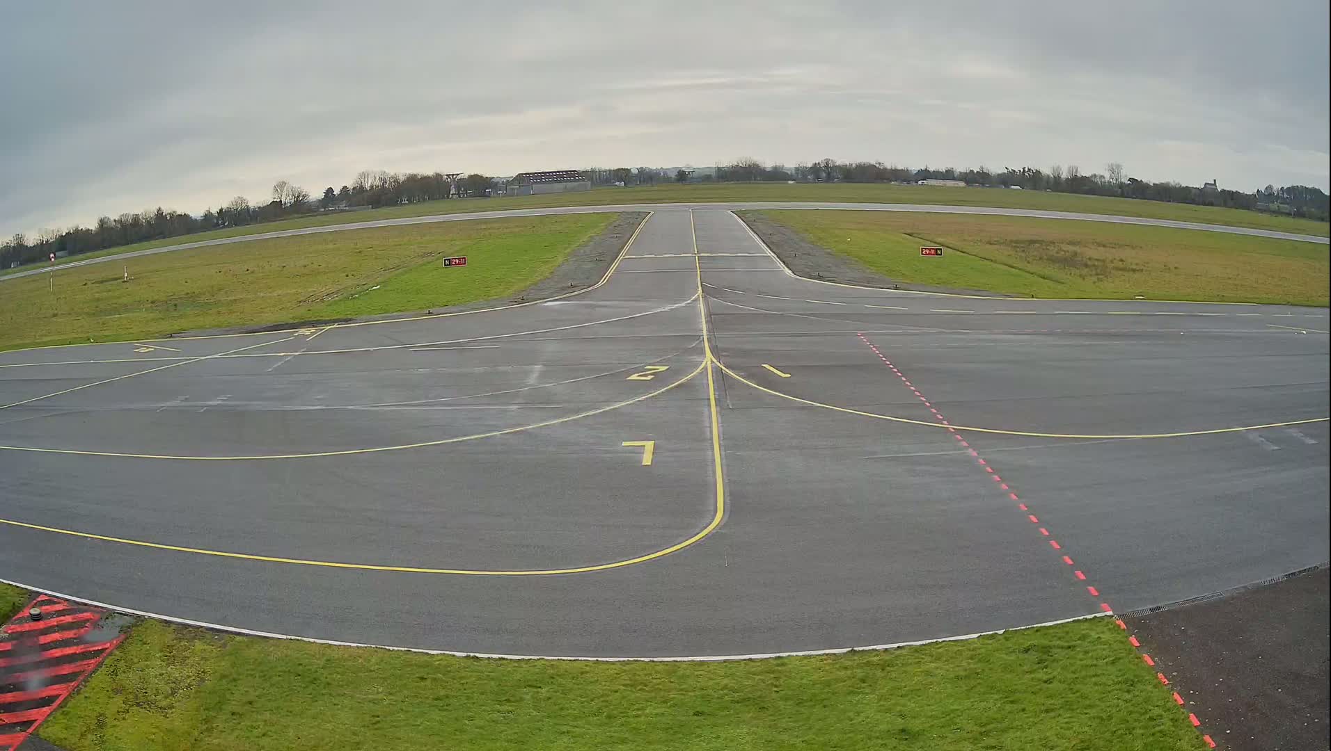 An overcast day reveals an airport tarmac with numbered taxiways leading to a runway bordered by grassy fields.