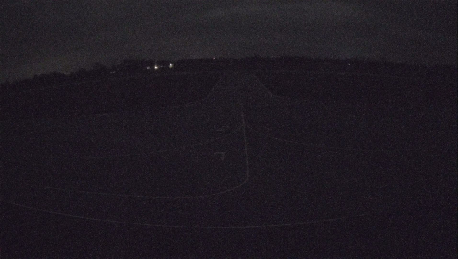 A dark, nighttime view of a paved area with faint lines, possibly a road or airfield, under a cloudy sky.
