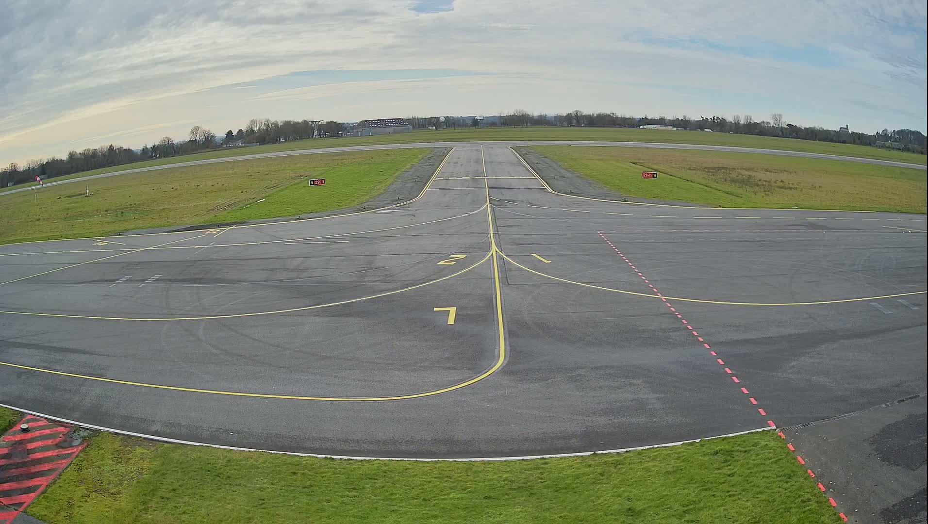 An airport tarmac with yellow lines marking taxiways and runways under a cloudy sky.