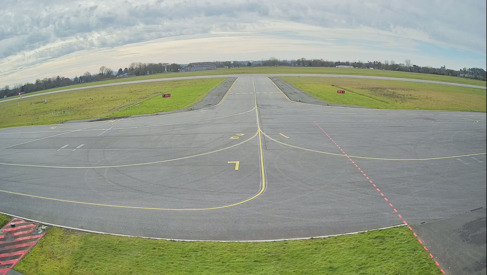 An airfield apron with taxiway markings under a cloudy sky.