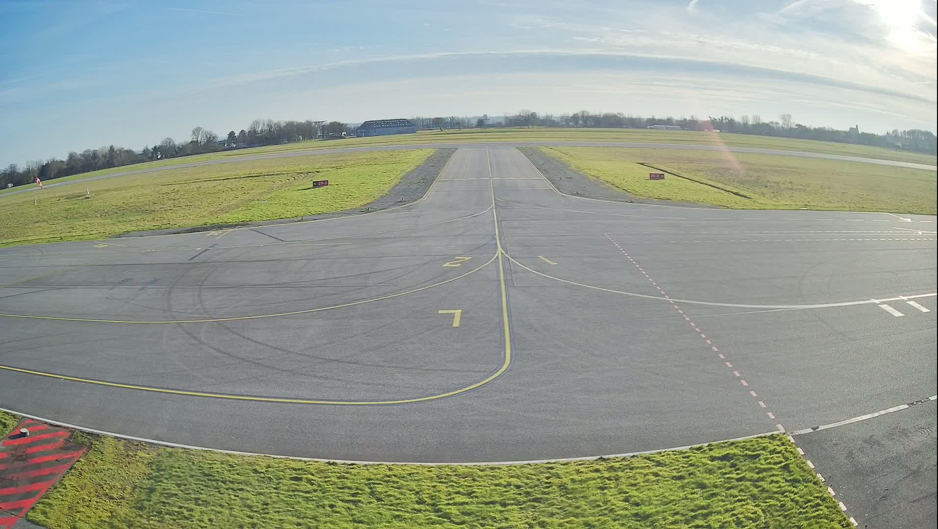 A tarmac airport runway and taxiway intersect under a clear, sunny sky.