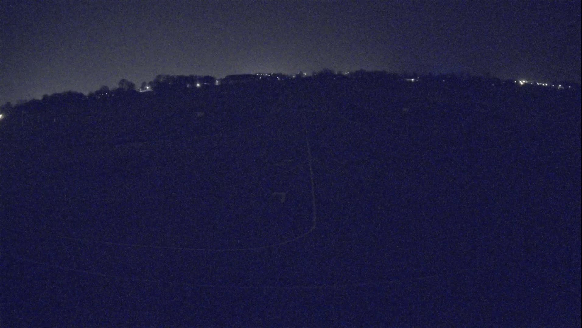 A dark, nighttime view of a hilltop with sparsely-lit buildings and a mostly-dark landscape.